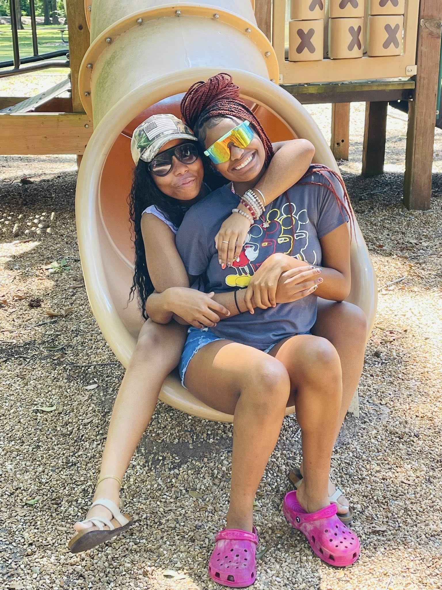 Two teenage girls sitting on the end of a slide.